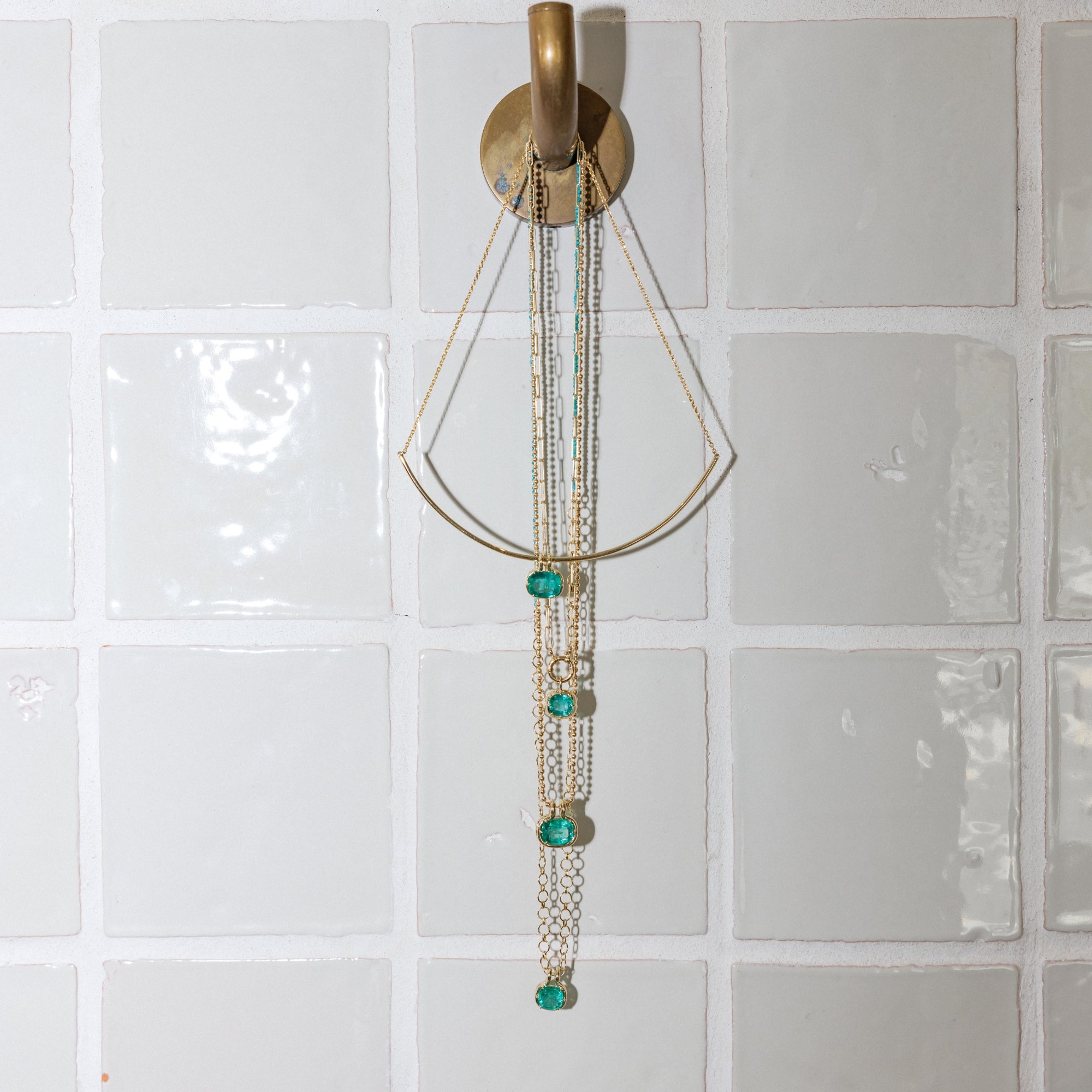 14k Solid Gold Fine Jewelry Emerald Pendants On Gold Chain Hanging From Bathroom Hook Styled Lifestyle Shot