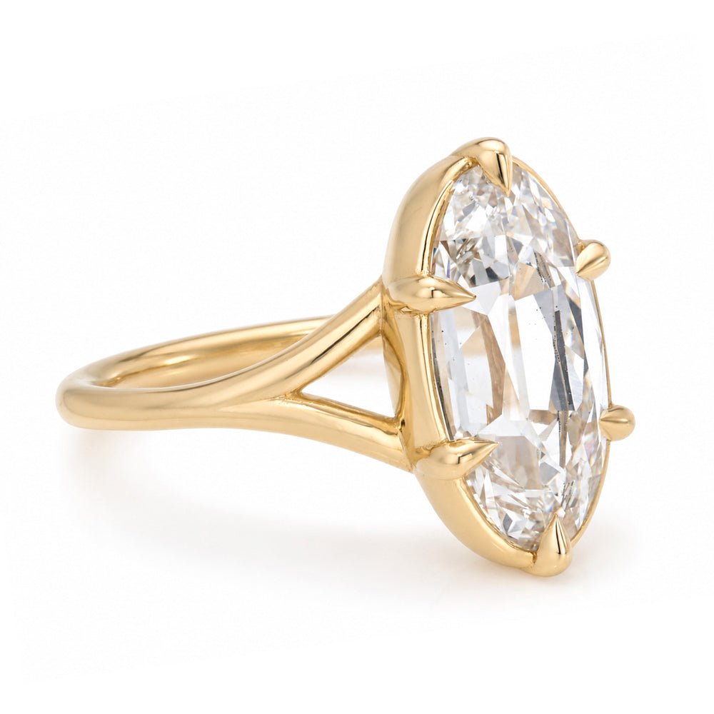 A yellow gold solitaire engagement ring featuring a moval old mine-cut white diamond in a bezel and 6 claw prong split shank setting, shown on a clean white background.