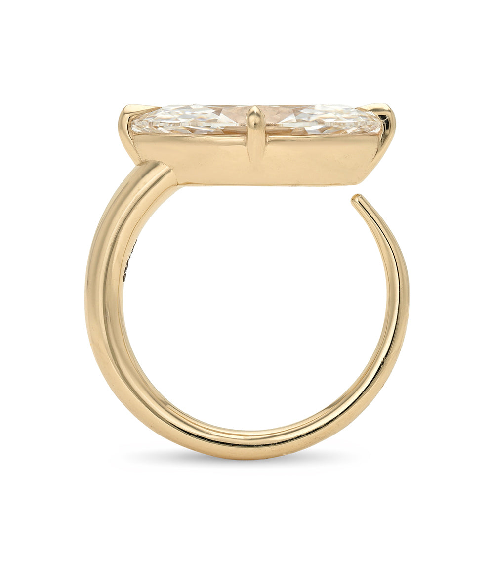 A yellow gold ring with a wide, flat top and a marquise-cut clear gemstone, shown on a plain white background.