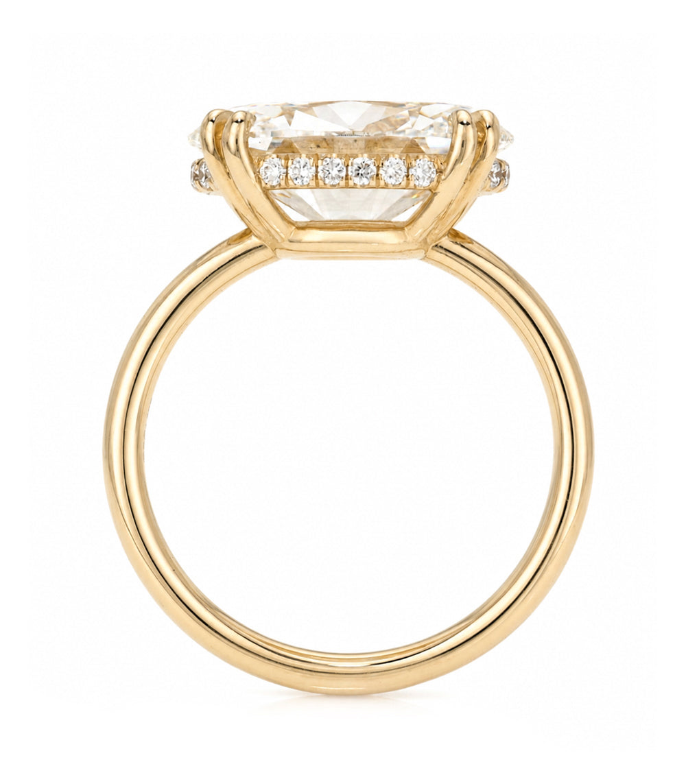 A yellow gold solitaire engagement ring featuring a oval brilliant cut white diamond set east west in a prong setting with a hidden halo on the basket and double prongs, shown on a clean white background.