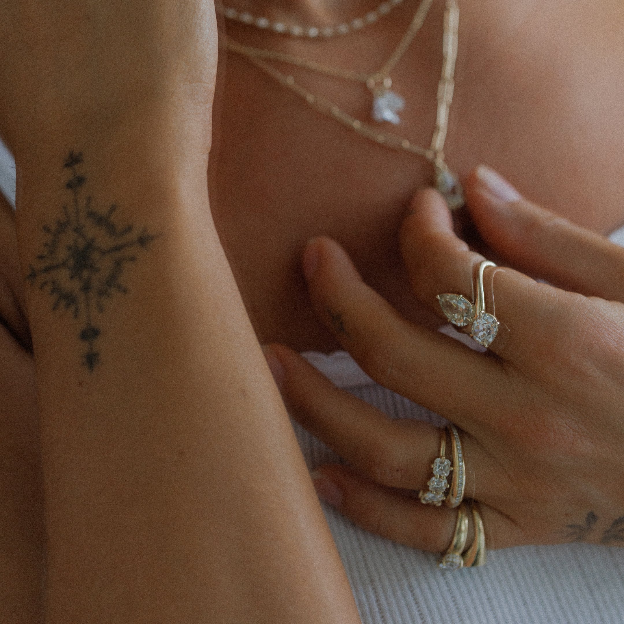tattooed hand touching diamond necklace pendant wearing gold rings with diamonds and stacked necklaces