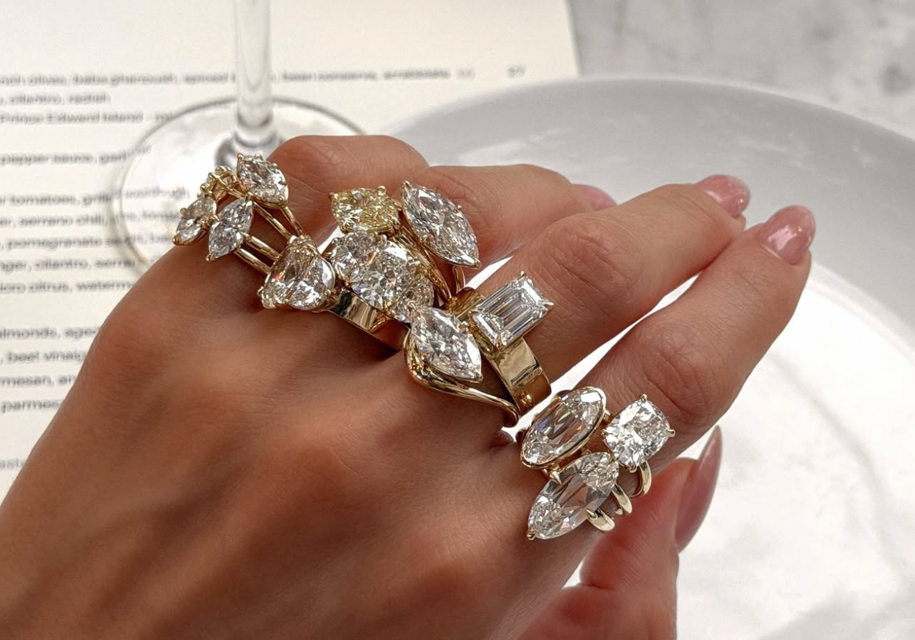 Hand wearing multiple diamond rings with a glass of wine in the background