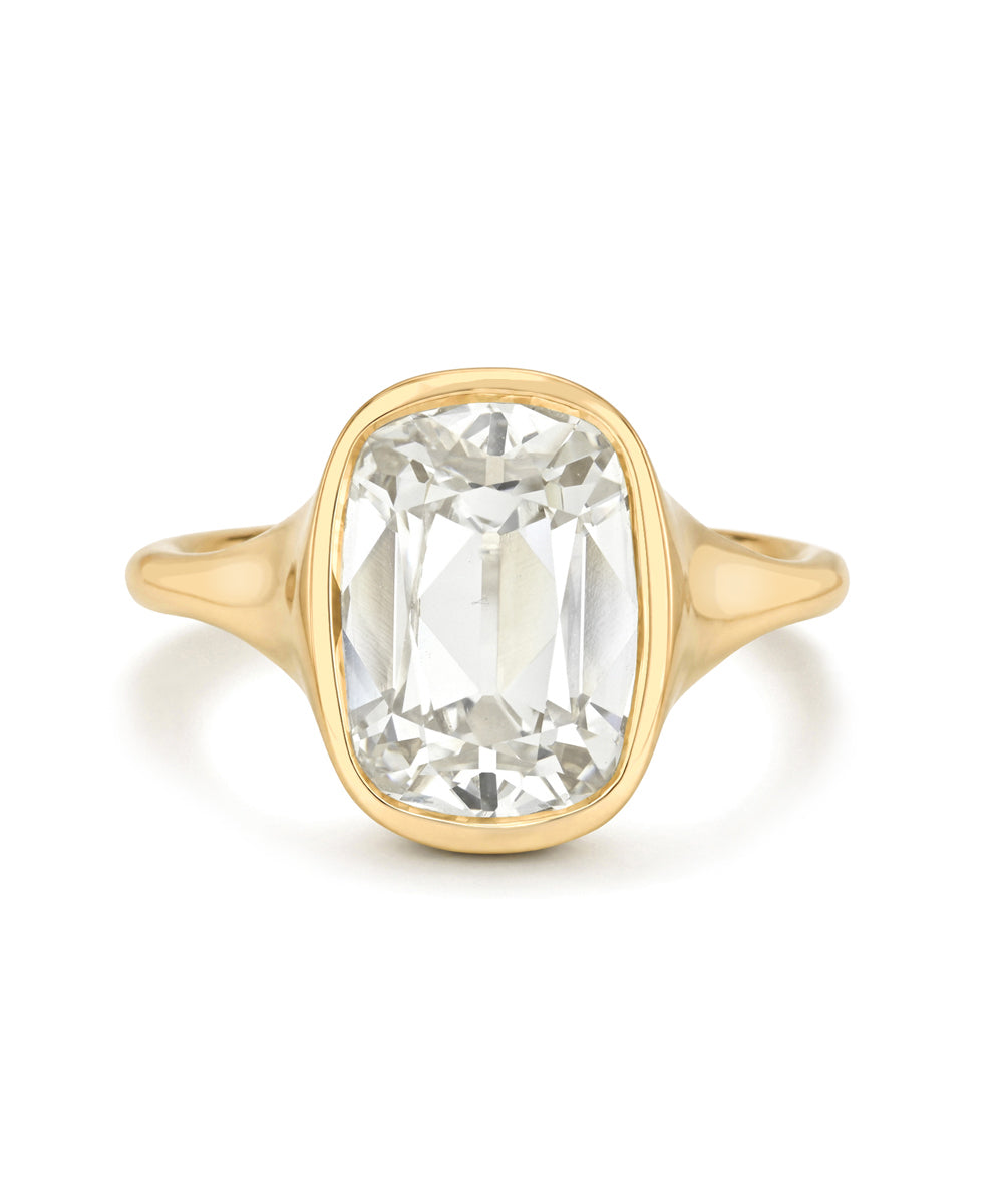 A yellow gold ring featuring a large cushion-cut white diamond in a bezel setting, shown against a plain white background.
