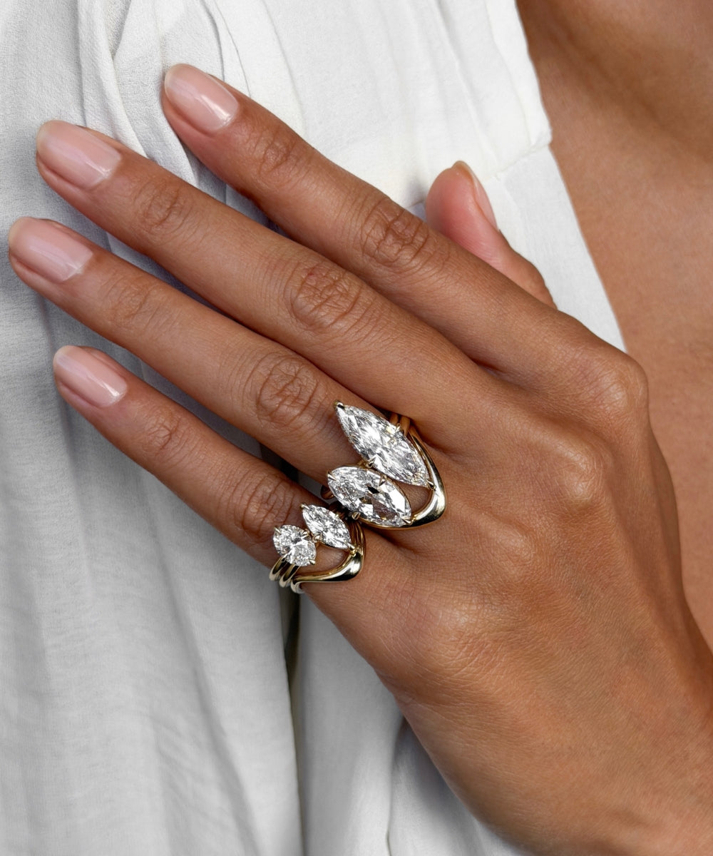 A close-up of a hand wearing a gold ring set with marquise-cut clear gemstones, resting against a white garment.