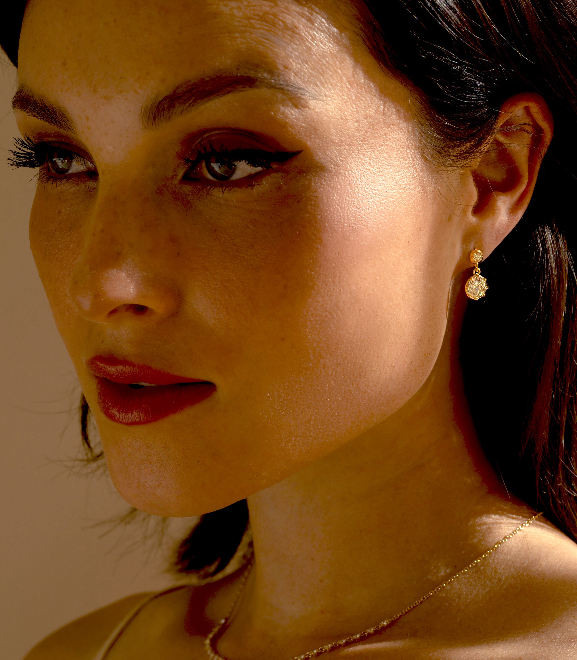 Woman’s side profile with a close-up gaze, wearing gold drop earrings featuring a round diamond