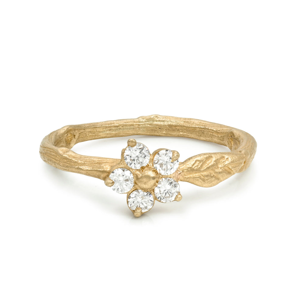 A gold ring featuring a textured, branch-like band with a small flower motif set with five clear round-cut gemstones, photographed on a clean white background.