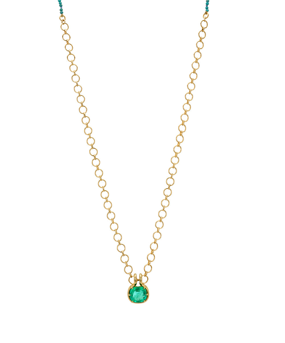 A delicate gold loop chain necklace with a small, elongated cushion green emerald pendant, displayed against a solid white background.