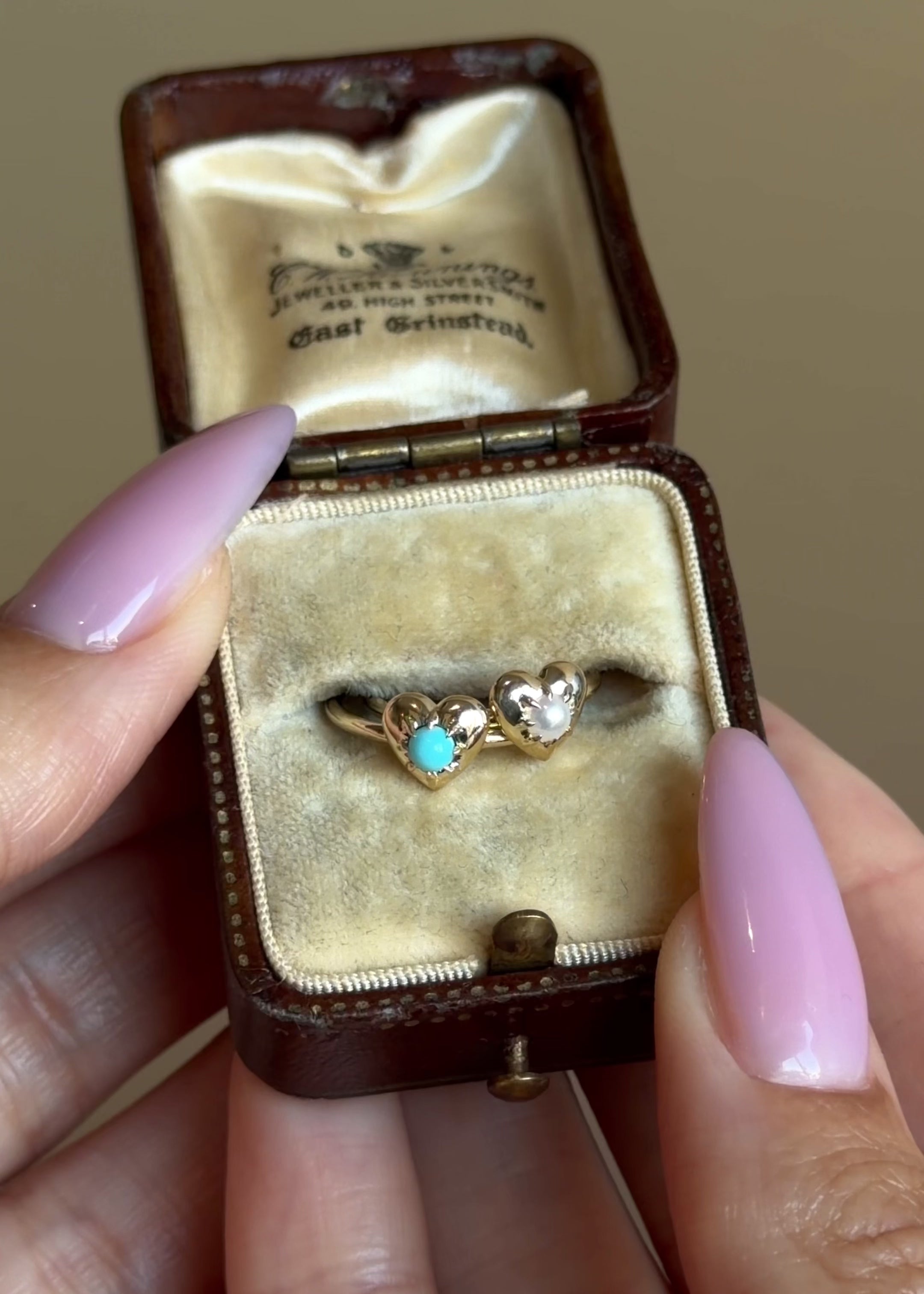Two heart pinky rings featuring a turquoise and pearl gemstone on a thin 14k yellow gold band shown in a box with hands.
