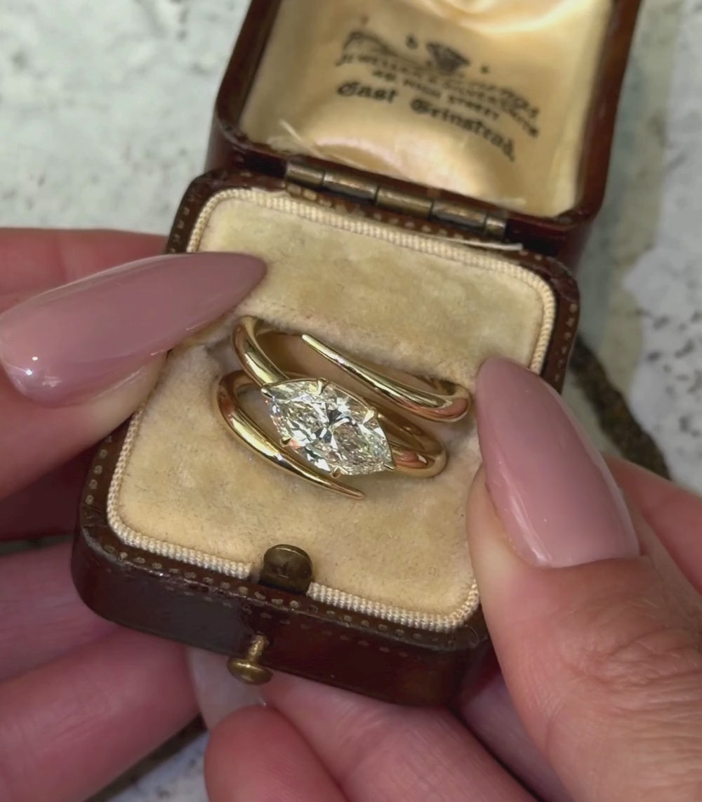 14K yellow gold triple coil ring with a 2.01ct pear shaped brilliant cut champagne diamond set in a tilted orientation in a engagement ring setting shown in a box with hands.