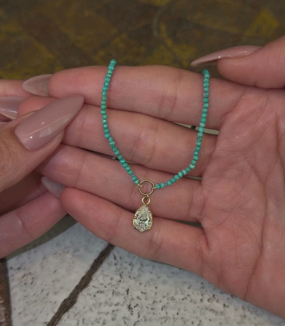 Turquoise beaded necklace with a 14k yellow gold pear brilliant pendant shown with hands.