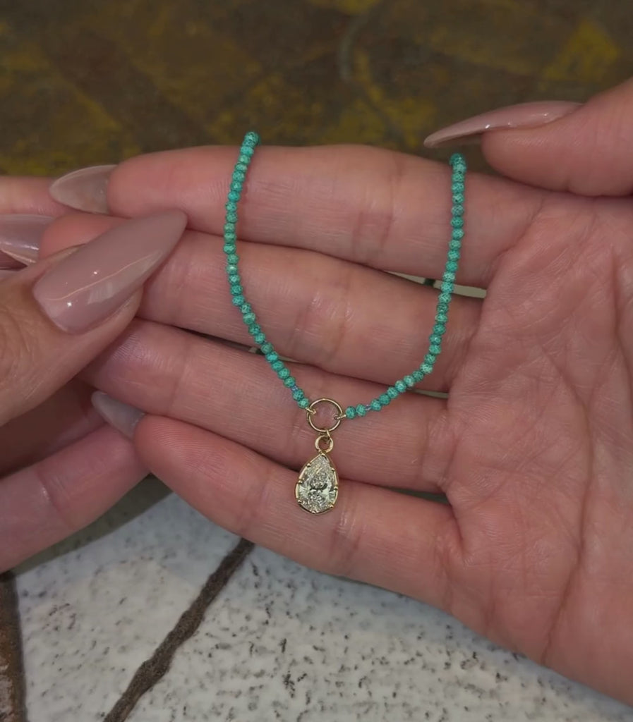 Turquoise beaded necklace with a 14k yellow gold pear brilliant pendant shown with hands.