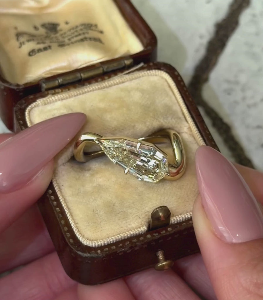14K yellow gold ring with a 3.21ct pear shaped step cut champagne diamond set in a tilted orientation in a engagement ring setting shown in a box with hands.