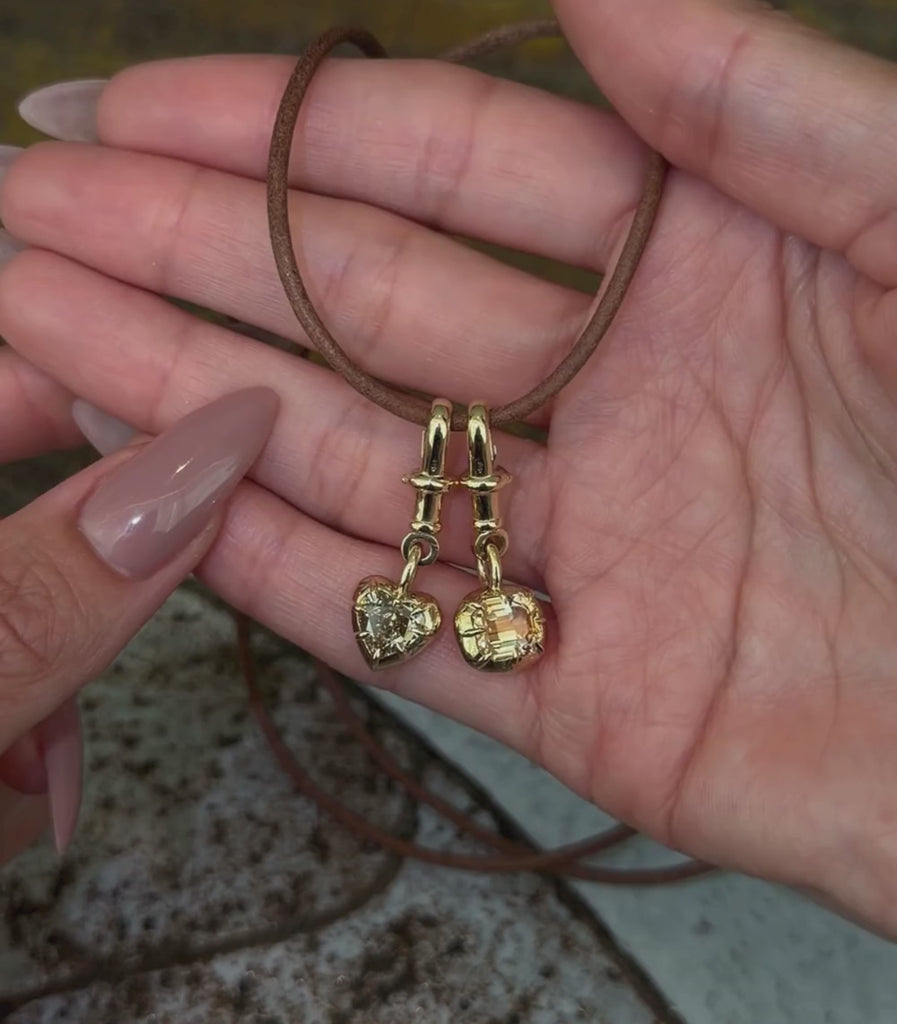 14K yellow gold heart shaped and emerald cut champagne diamond collet toggle pendants worn with a leather cord necklace and shown with hands.