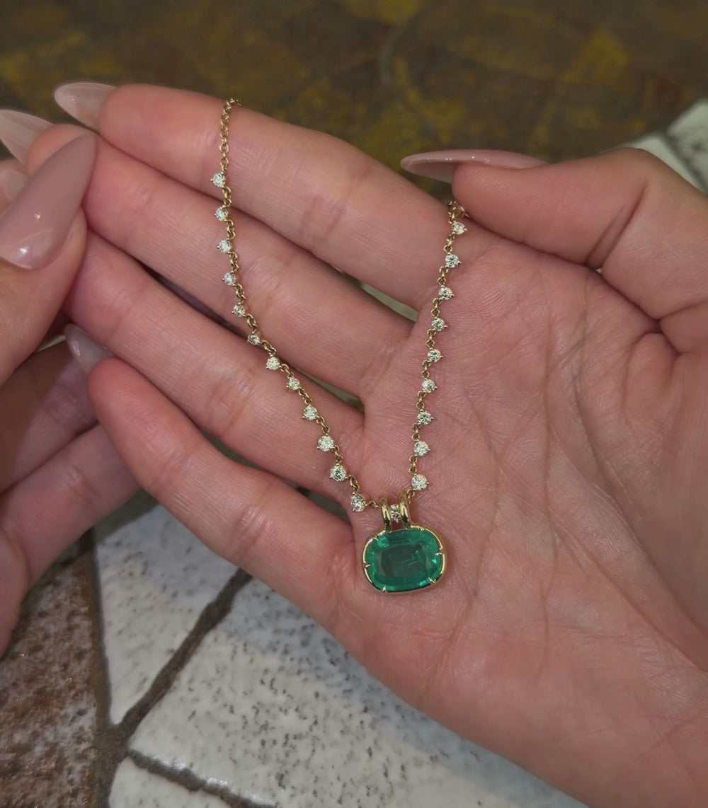 14k yellow gold chain necklace with half diamond station details and elongated cushion emerald pendant, shown with hands.
