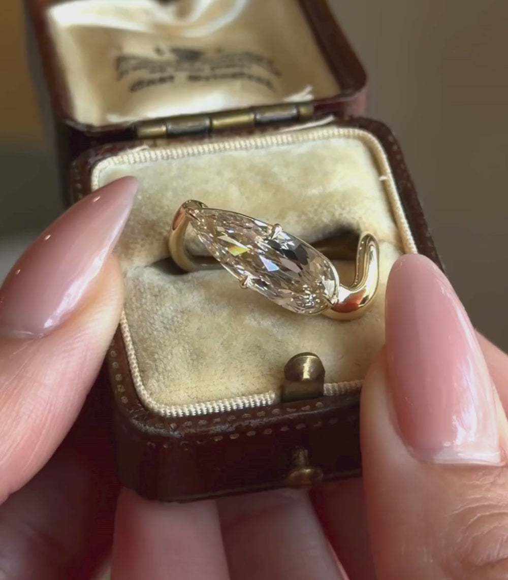 14K yellow gold ring with a 3.21ct pear shaped brilliant cut champagne diamond set in a tilted orientation in a engagement ring setting shown in a box with hands.