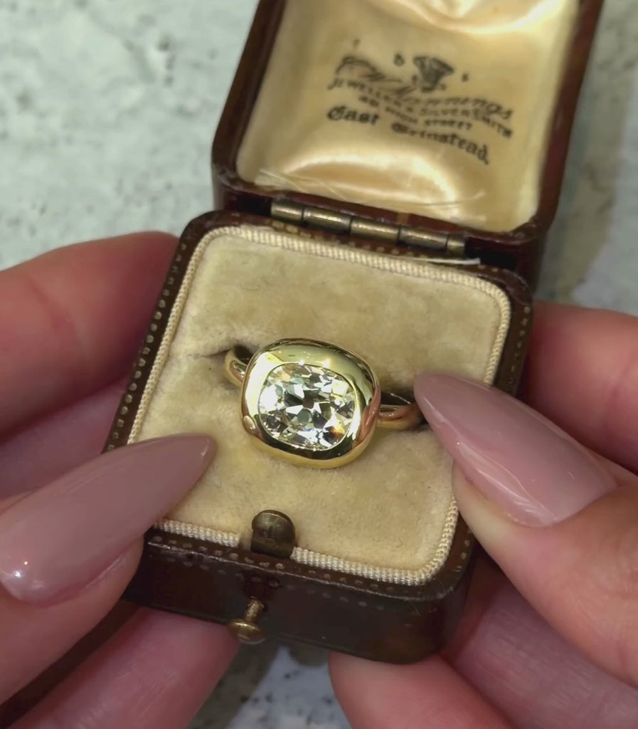 18K yellow gold ring with a 3.12ct elongated cushion old mine cut champagne diamond set east west in a engagement ring setting shown in a box with hands.