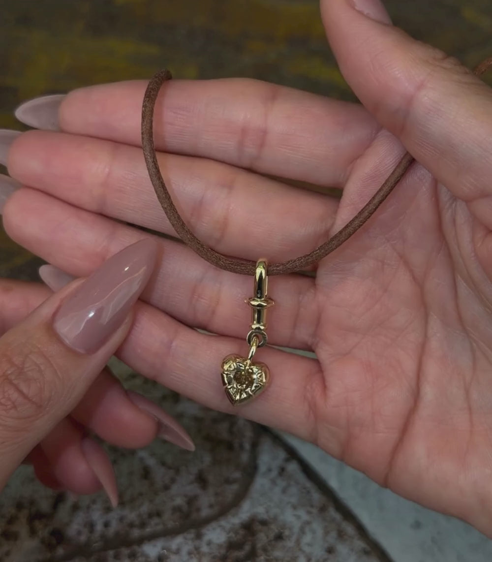 14K yellow gold heart shaped champagne diamond collet toggle pendant worn with a leather cord necklace and shown with hands.