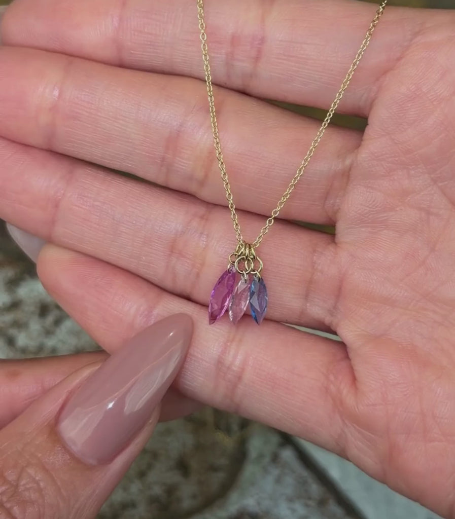 14K yellow gold chain necklace with three pear brilliant cut sapphire pendants in purple, pink and blue shown with hands.