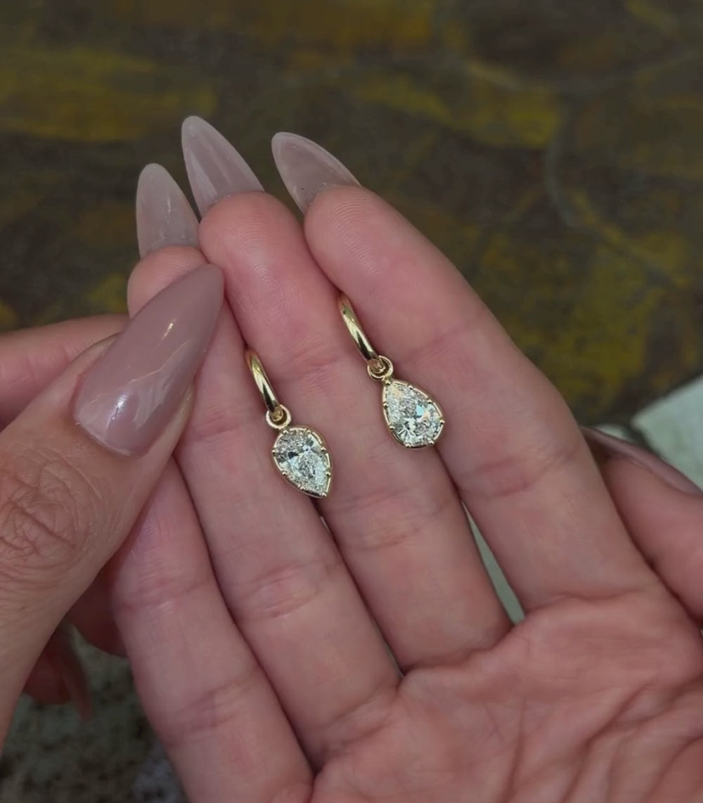 14K yellow gold hoop huggie earrings with alternating pear brilliant cut diamond dangle details, shown with hands.