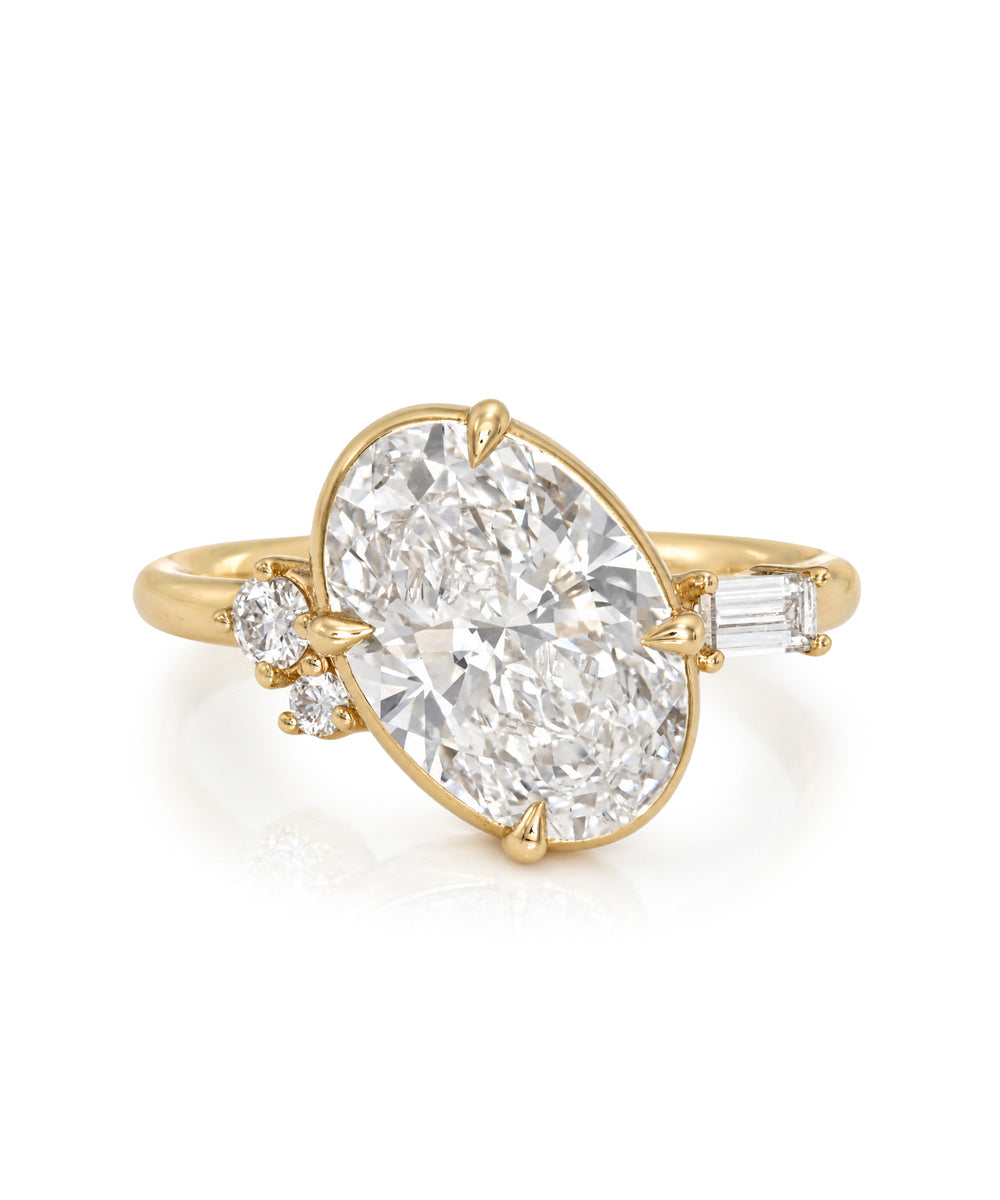 A yellow gold ring featuring a large oval-cut diamond center stone, accented by a small round diamond and an emerald-cut side diamond on a clean white background.